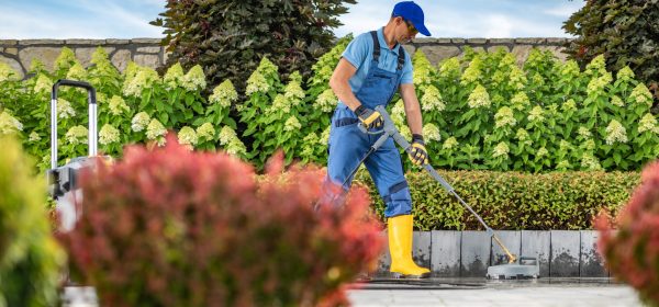 Caucasian Worker Power Washing Concrete Bricks Driveway Using Pressure Washer